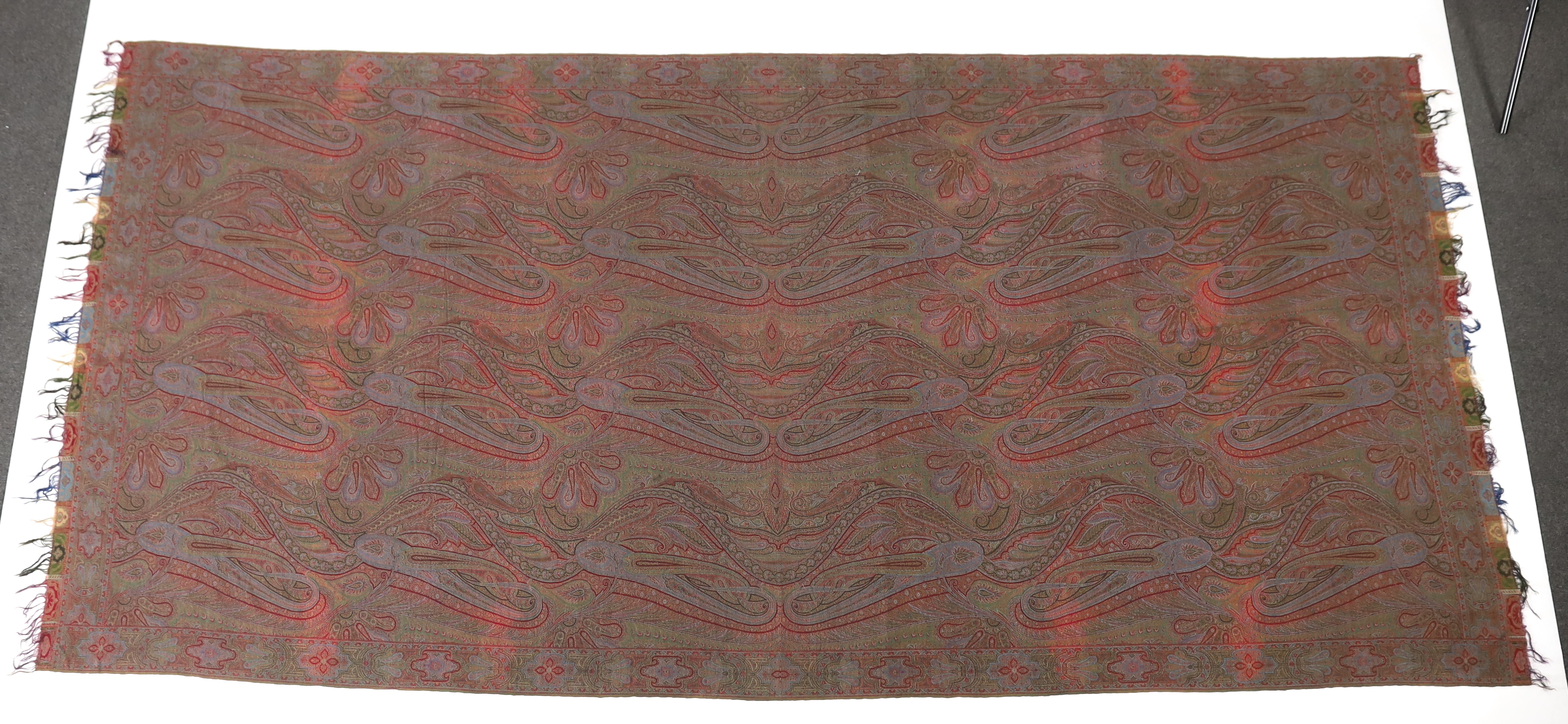 An 1860’s-70’s Scottish Paisley wool shawl, woven with multi coloured wools in a large scrolling teardrop design, bordered and fringed both ends 165cm wide x 345cm long
